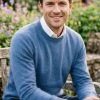 Man wearing Lona Scott pure Mongolian cashmere crew neck jumper in denim blue, styled with a white shirt in a beautiful garden setting – timeless gentleman’s knitwear
