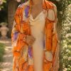 Woman wearing the Oranges & Figs pure silk chiffon stole in warm orange and fig tones over an ivory silk dress in a Mediterranean-style rose garden.