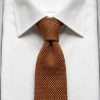 Burnt orange silk knitted tie knotted on white dress shirt collar