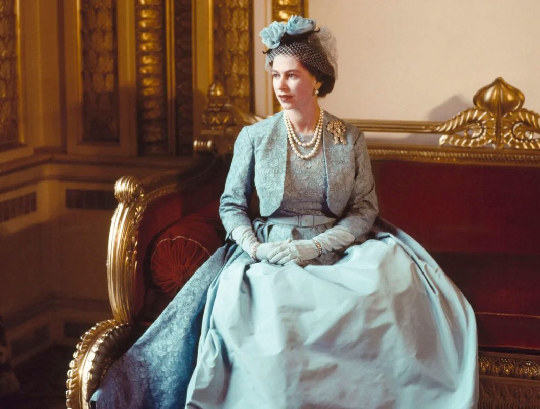 Queen Elizabeth II: Her Life in Style exhibition. The Queen in a pale blue Norman Hartnell gown and matching hat, seated in a formal portrait that features in the exhibition at The King’s Gallery, Buckingham Palace.